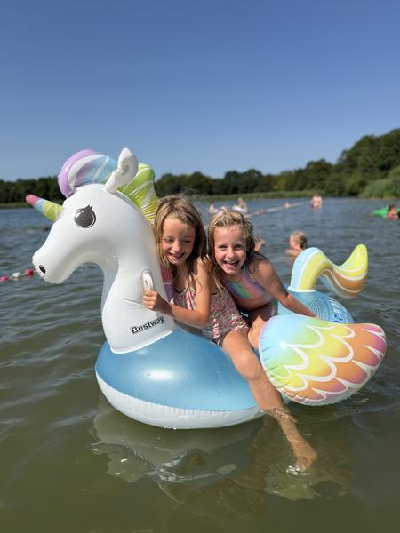 Two girls sitting on an inflatable unicorn float in a lake on a sunny day